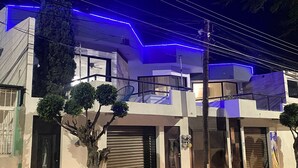 Un bâtiment moderne à deux étages, doté d’un balcon, avec un arbre devant et une voiture garée.