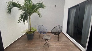 Une petite terrasse avec un palmier, deux chaises et une table.