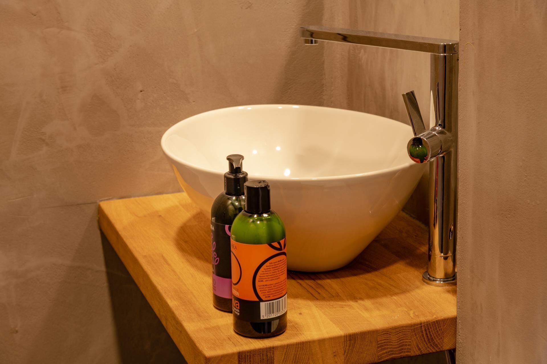 Une salle de bain avec un grand lavabo blanc, un meuble-lavabo en bois et deux flacons de savon liquide posés sur le comptoir.