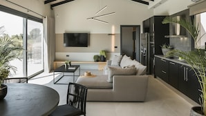 A modern living room with a large TV, sofa, and dining area. - Single-Storey Contemporary Villa, A/C, Private Pool and Panoramic Sea Views - 10 mins to Beaches (Avithos)