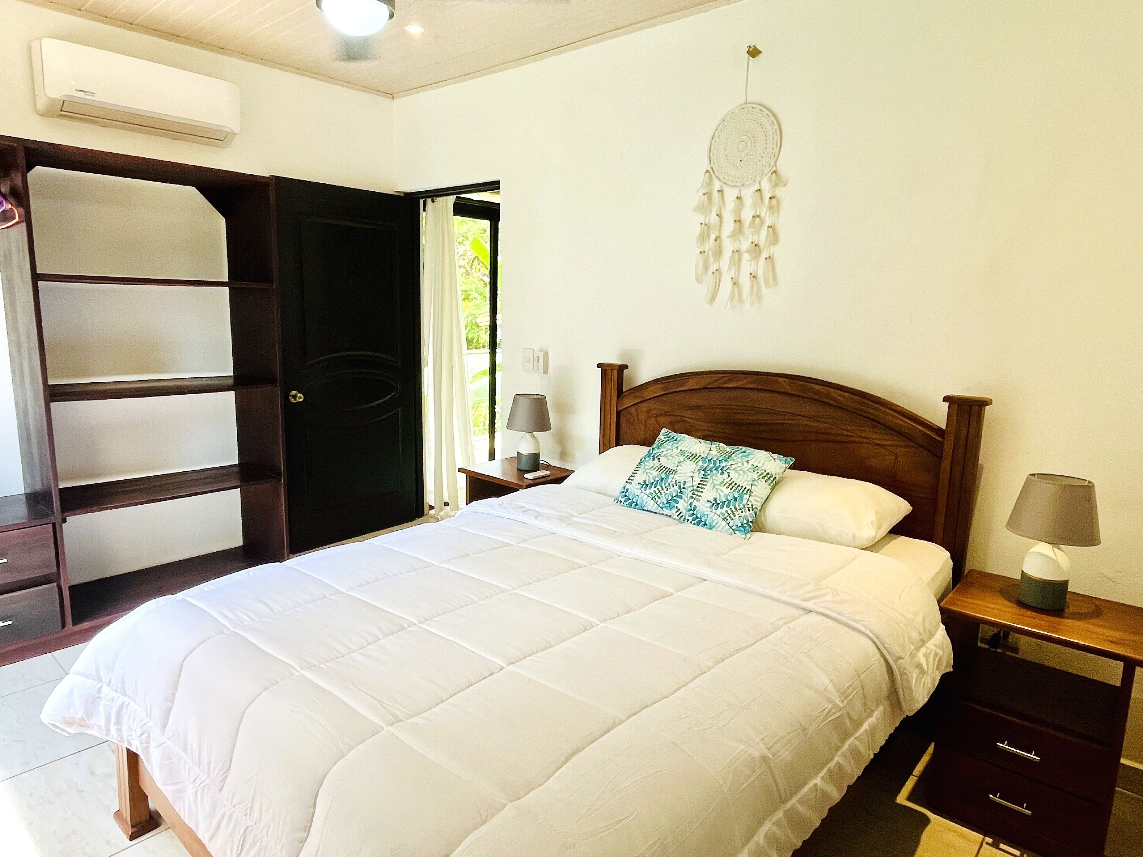 Quarto com cama, mesas de cabeceira, guarda-roupa e um apanhador de sonhos na parede.
