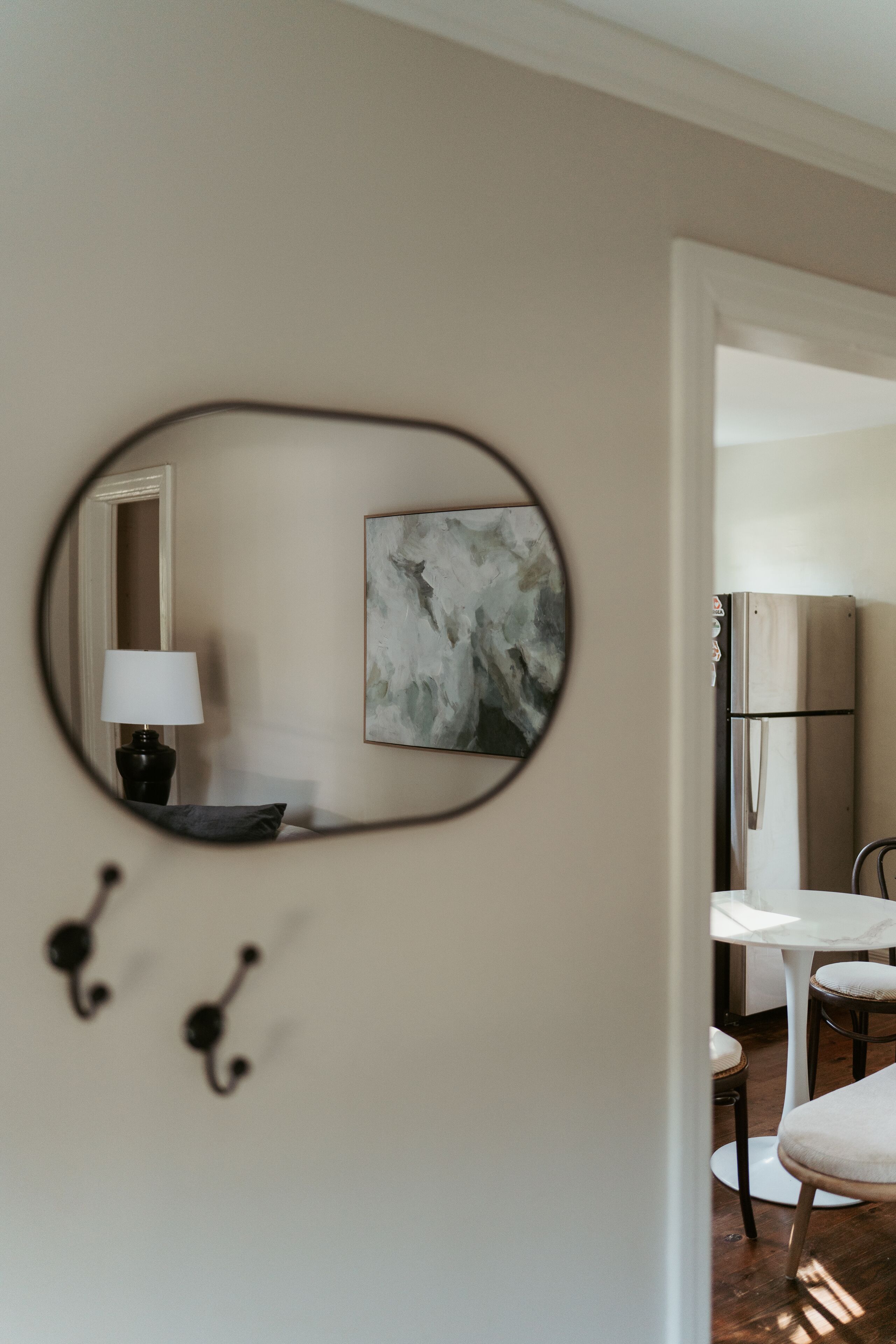 A modern interior with a round mirror, abstract art, a lamp, and a dining area.