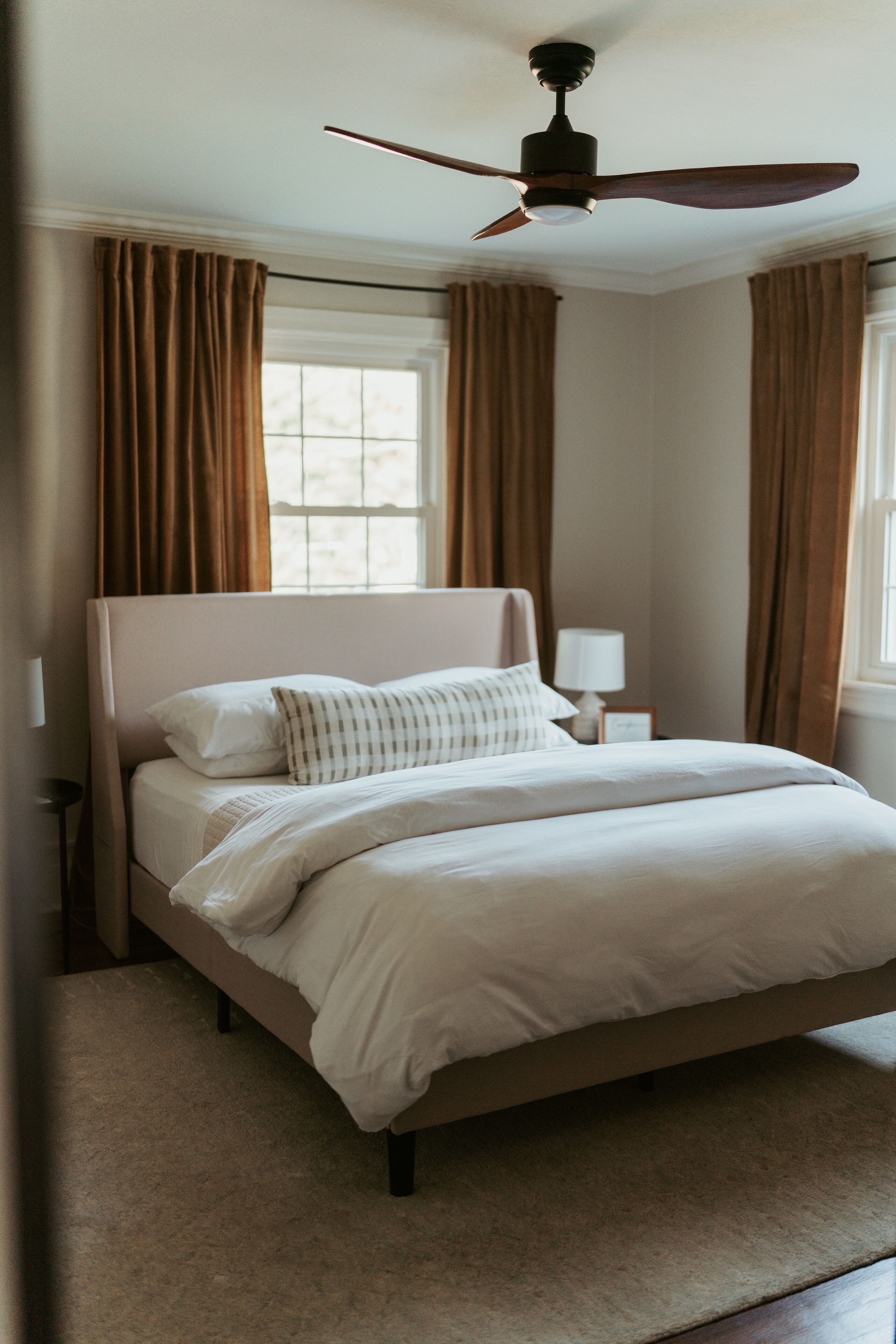 A bedroom with a bed, a ceiling fan, a nightstand, and a window with curtains.