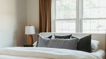 A bedroom with a bed, a ceiling fan, a window with curtains, and a nightstand with a lamp.