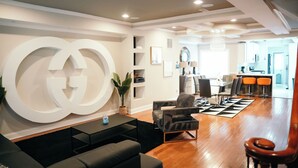A modern living room with a large white logo on the wall, a black sofa, and a wooden floor.