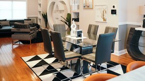 A modern living room with a dining area, featuring a chandelier, contemporary furniture, and a geometric patterned rug.