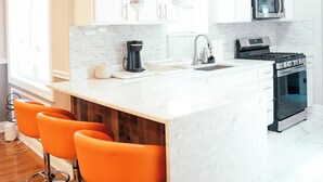 A modern kitchen with white cabinets, a large island with bar stools, a microwave, stove, and a coffee maker.