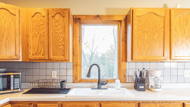 A kitchen with wooden cabinets, a white sink, a window, and a coffee maker. - Lakeside Luxury on Upper & Lower Post Lake Channel (Post Lake)
