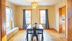 A dining room with a wooden table, chairs, a chandelier, and a window with curtains. - Lakeside Luxury on Upper & Lower Post Lake Channel (Post Lake)