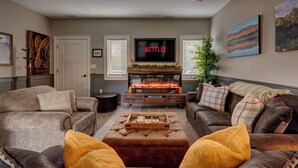 A cozy living room with a fireplace, leather sofas, and a flat-screen TV displaying 'NETFLIX'. - Escape Route Retreat · Town Center Retreat* Hot Tub, Game Room, Fire Pit (Lincoln)