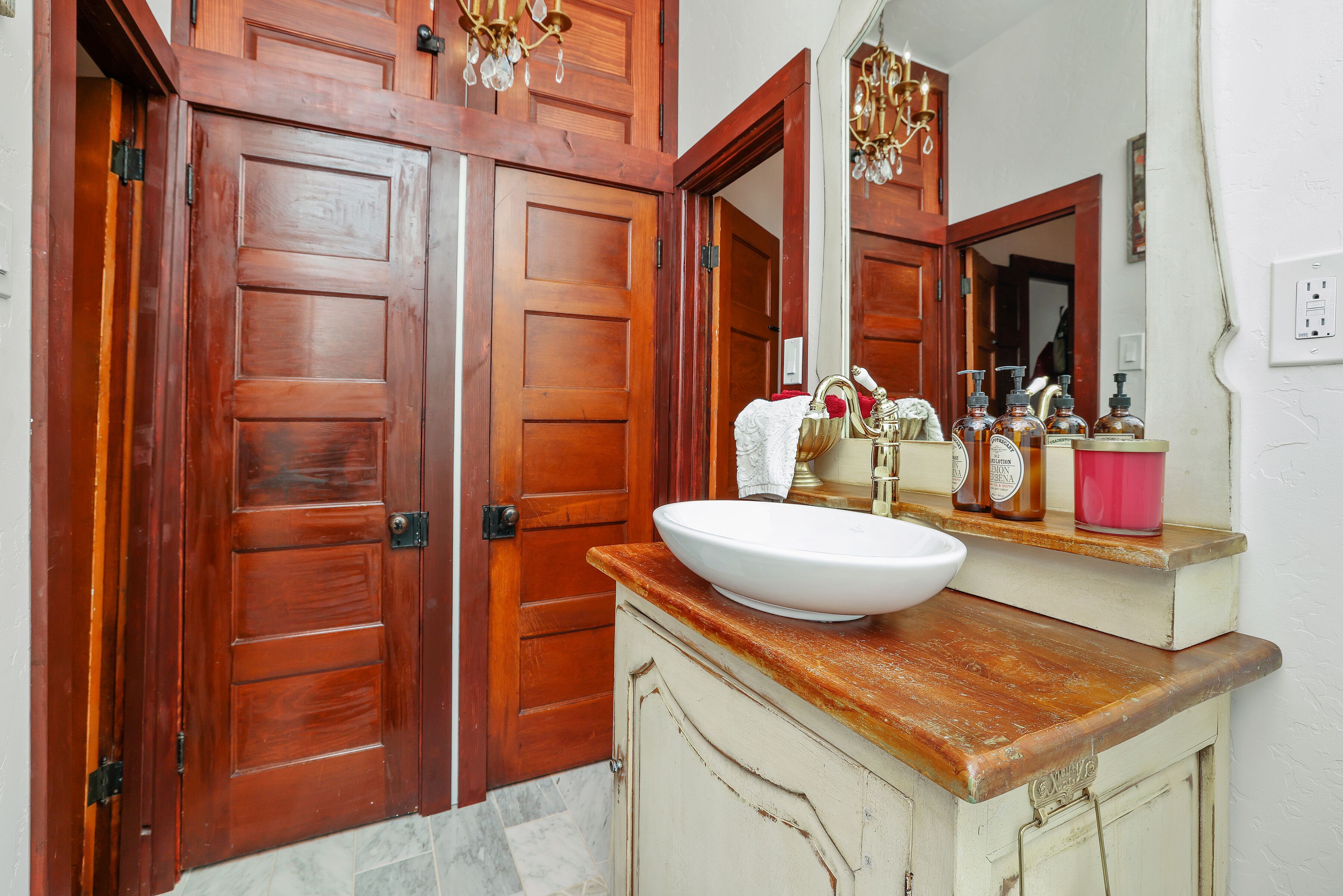 Un baño con puerta de madera, un lavabo blanco y un espejo encima.