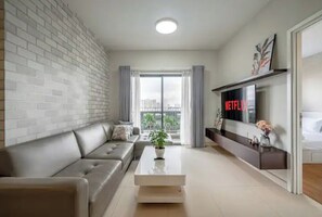 A modern living room with a sofa, a coffee table, a TV mounted on the wall, and a city view through the window.