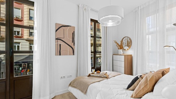 Une chambre moderne avec un grand lit, une table de chevet avec une lampe et une vue sur la ville grâce à de grandes fenêtres du sol au plafond.