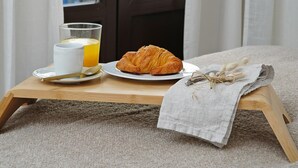 Une table en bois dressée pour le petit-déjeuner, avec un croissant, une tasse et un verre de jus d’orange.