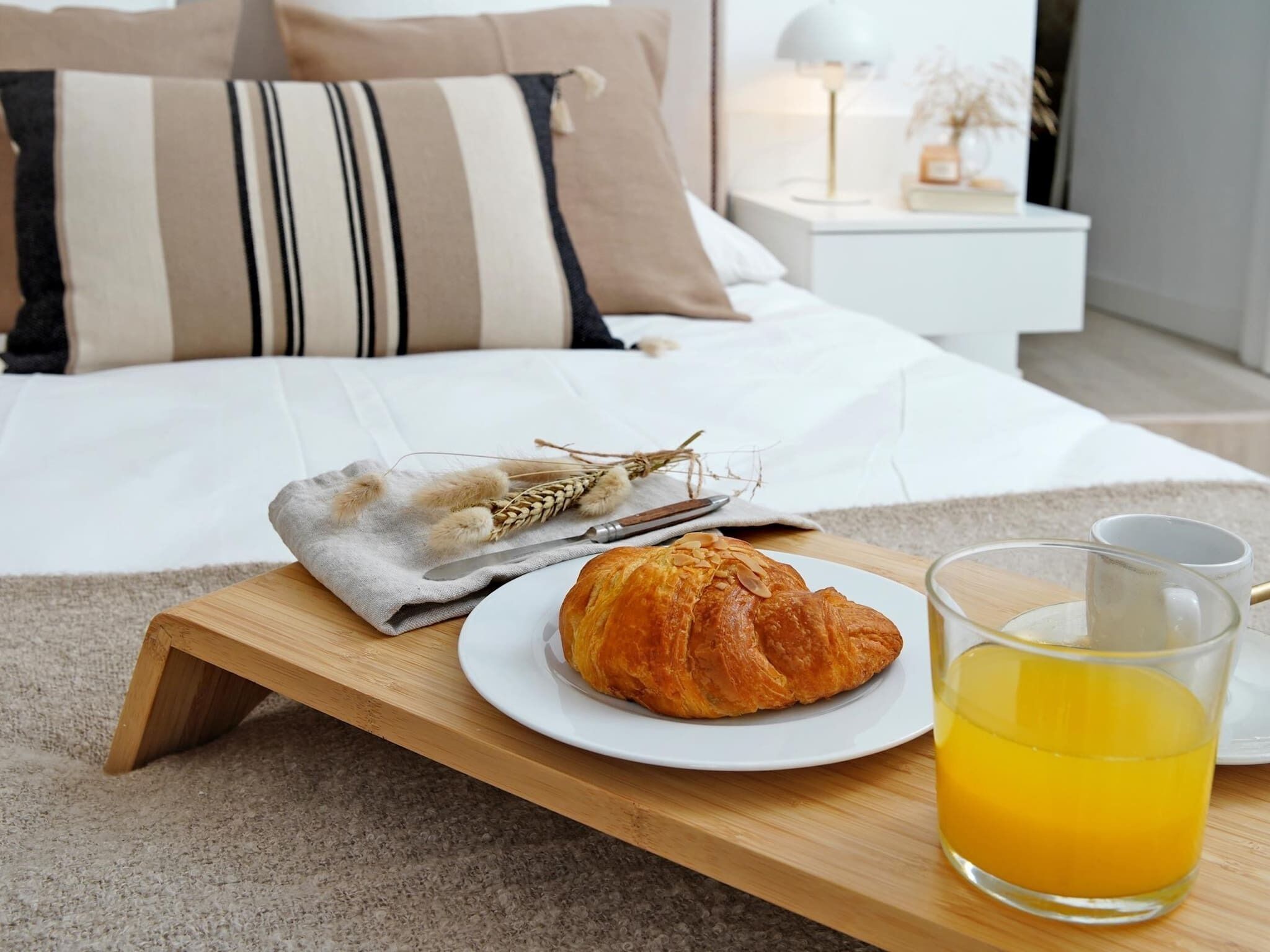 A breakfast tray with a croissant and a glass of orange juice on a wooden table in a hotel room.