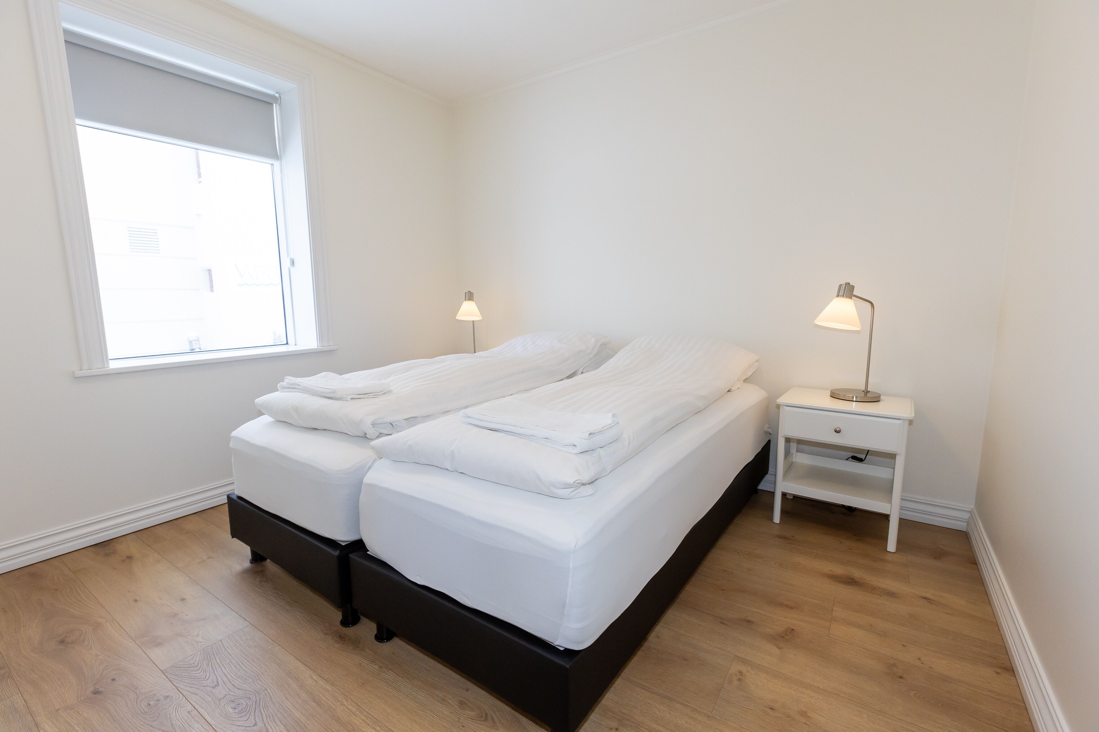 A bedroom with a bed, two bedside tables, a window, and a nightstand.