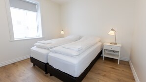 A bedroom with a bed, two bedside tables, a window, and a nightstand. - Hrimland Guesthouse (Akureyri)