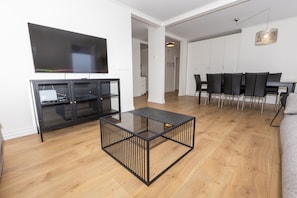 A modern living room with a glass coffee table, a flat-screen TV, and a dining area with a black table and chairs. - Hrimland Guesthouse (Akureyri)