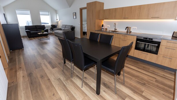 A modern kitchen with wooden cabinets, a dining table with chairs, and a visible oven. - Hrimland Guesthouse (Akureyri)