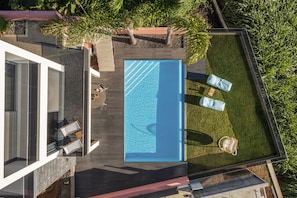 An aerial view of a modern house with a rectangular swimming pool, surrounded by a well-maintained lawn and a few trees. - With pool and superb sea view - Villa Candelária (Ponta do Sol)
