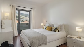 A modern bedroom with a large bed, bedside tables, and a view of a cityscape through a glass door. - City Holidays in Madeira - Madalenas XXI (Funchal)