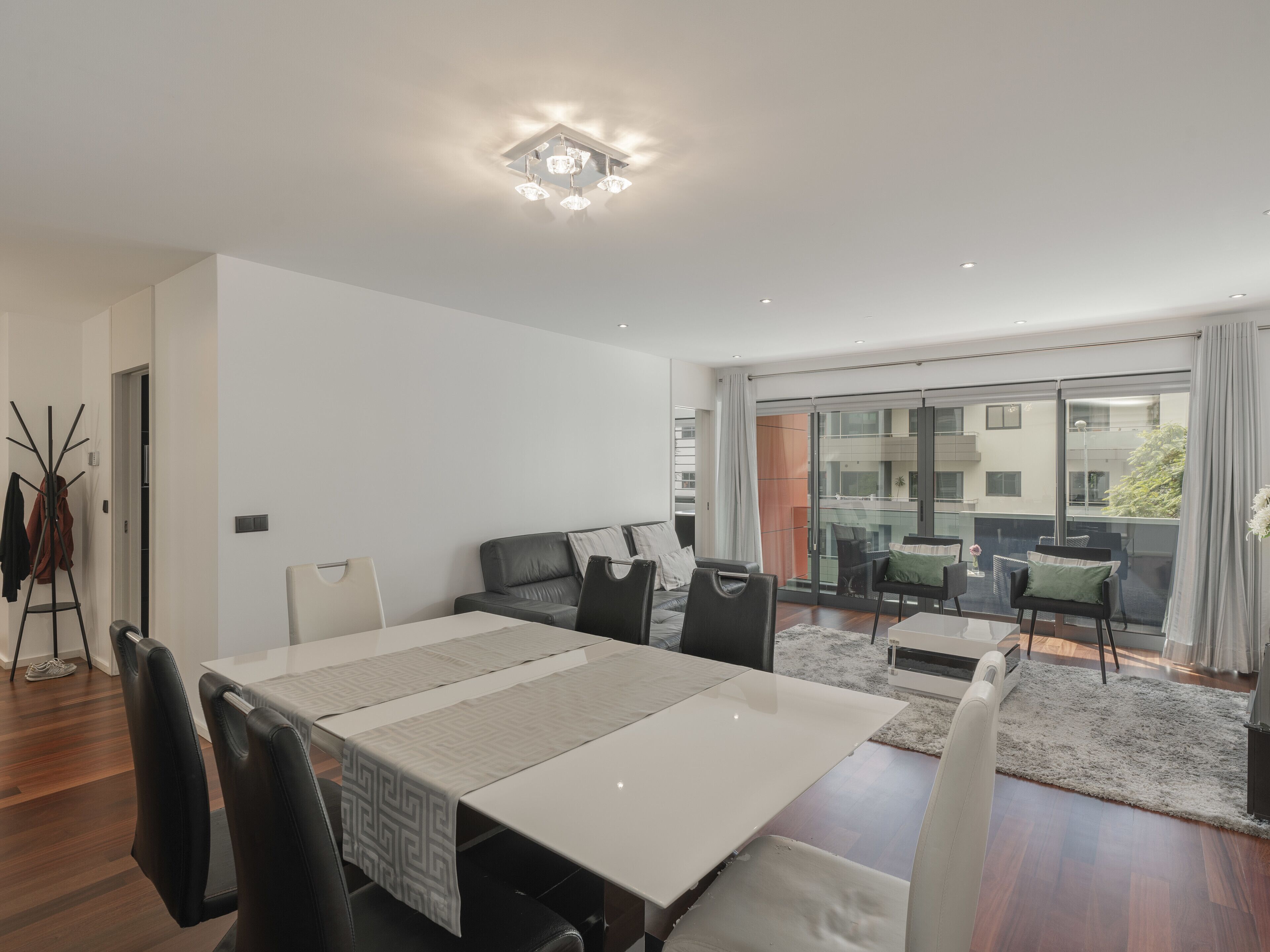 A modern dining room with a large table, black chairs, and a view of a balcony with outdoor seating.
