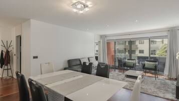 A modern dining room with a large table, black chairs, and a view of a balcony with outdoor seating.