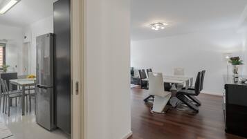 A modern kitchen with a refrigerator, a dining area with a table and chairs, and a hallway leading to another room.