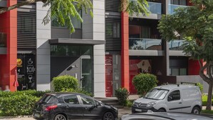 A modern building with a glass facade, numbered floors, and a restaurant sign indicating a café and takeaway. - City Holidays in Madeira - Madalenas XXI (Funchal)