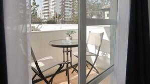 A balcony with a table and chairs, a potted plant, and a view of a tall residential building. - Hotel boutique Trinidad (Vina del Mar)