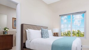 Habitación de hotel con cama, mesita de noche, ventana con vistas y puerta que da a otra habitación.