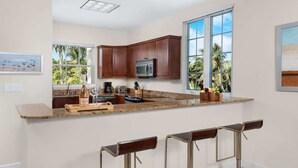 Una cocina moderna con una isla grande, taburetes de bar y vistas a palmeras.