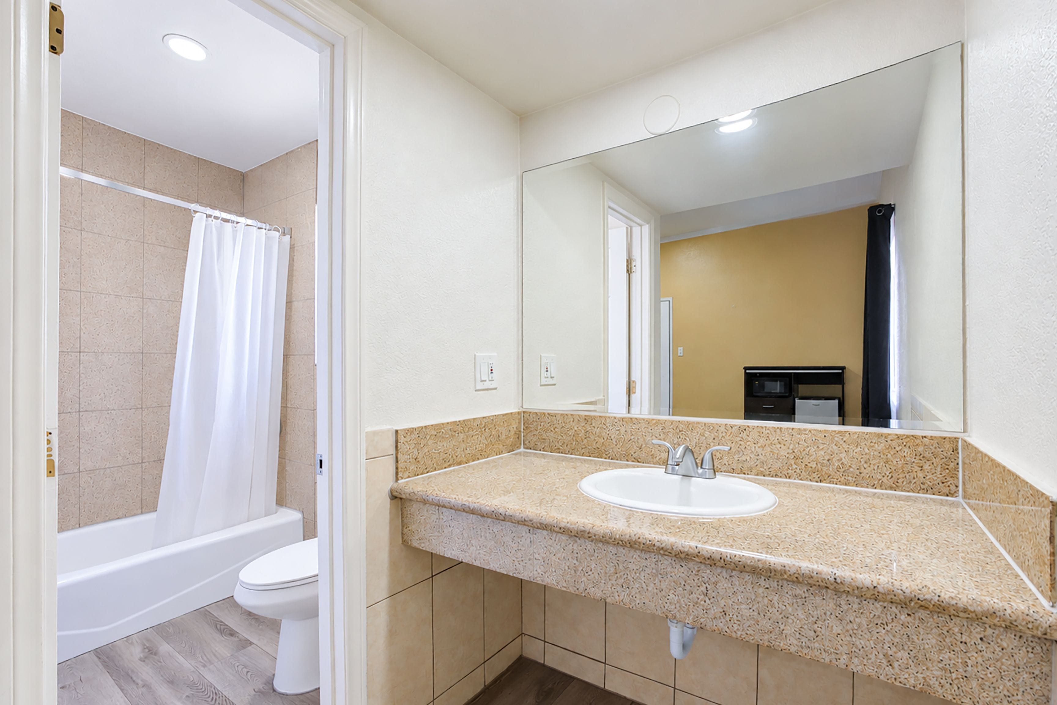 A bathroom with a white bathtub, a toilet, and a sink with a large mirror above it.