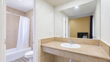 A bathroom with a white bathtub, a toilet, and a sink with a large mirror above it.
