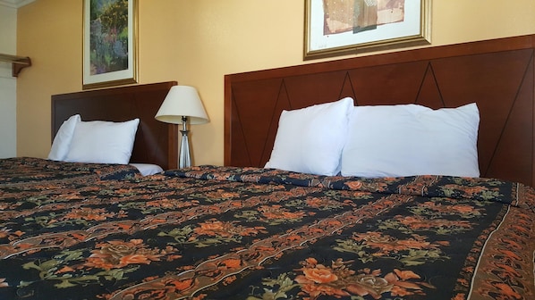 A hotel room with a large bed, two pillows, a nightstand with a lamp, and two framed pictures on the wall. - Royal Inn Motel, Compton CA (Compton)