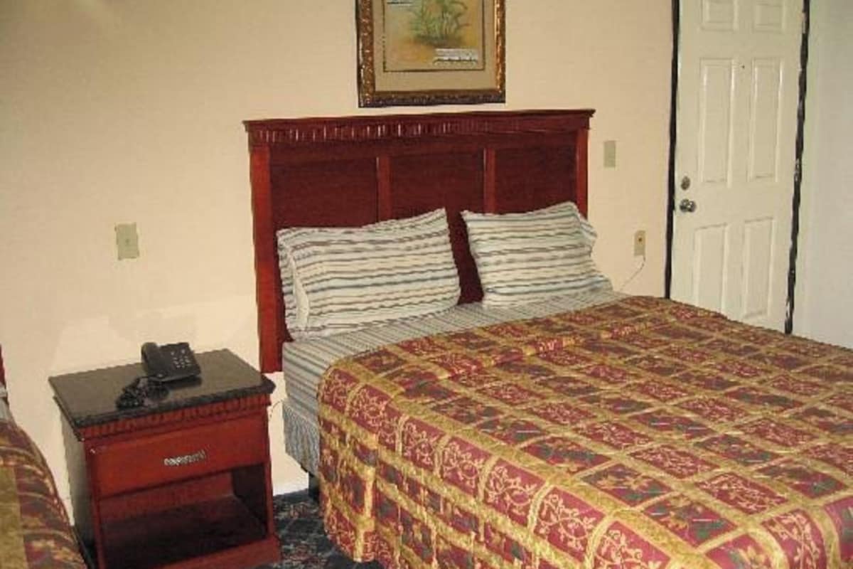A hotel room with a bed, a nightstand with a telephone, and a door.