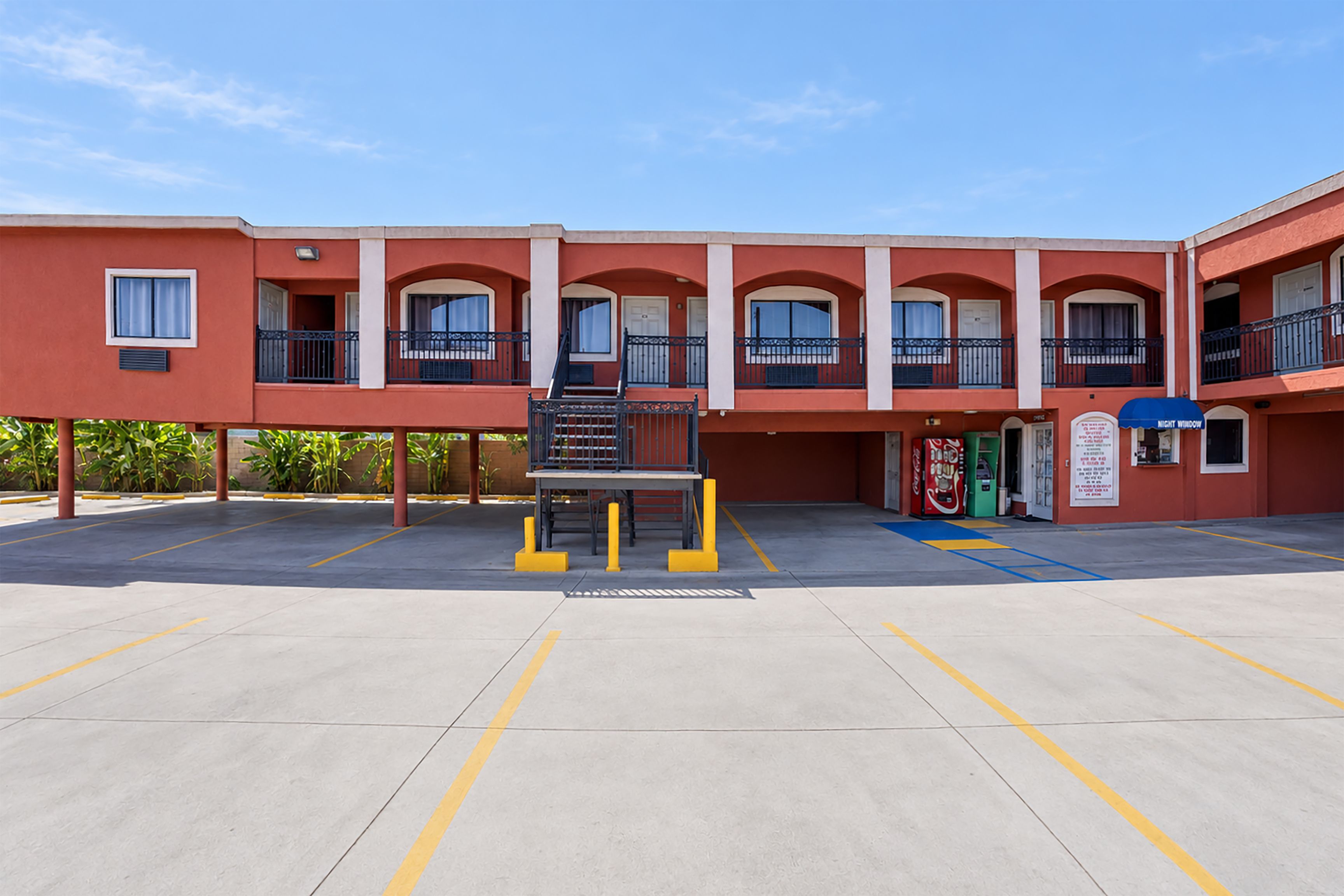 A building with a red facade, multiple balconies, and a parking area with yellow lines.