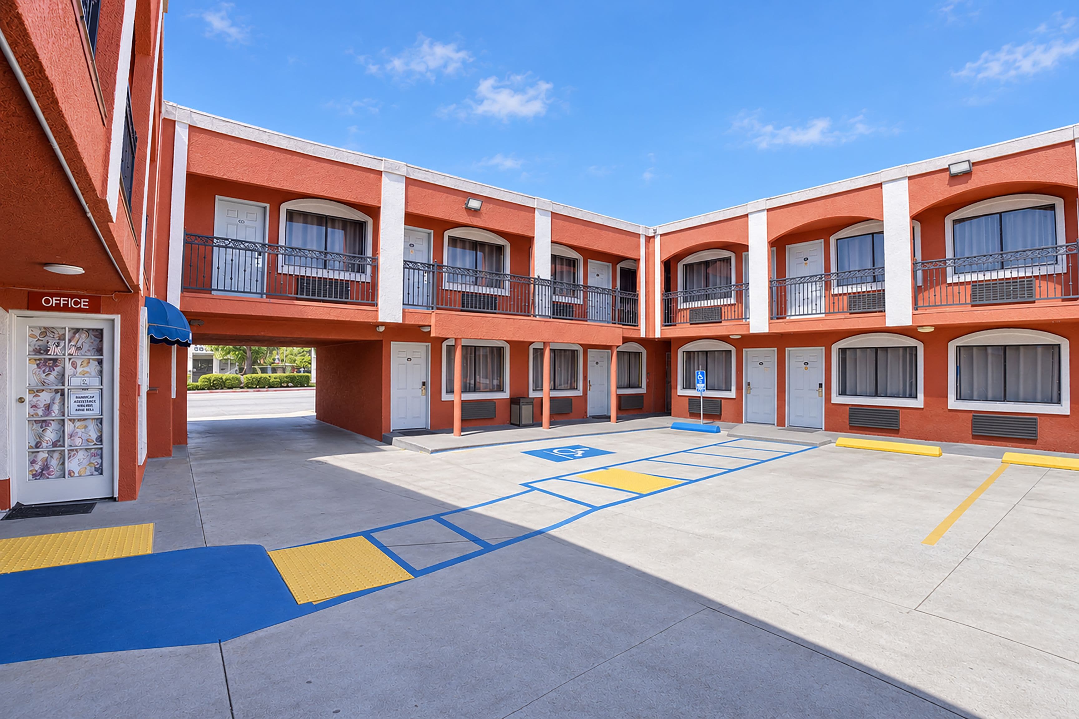 A multi-story building with a central courtyard, featuring a parking area with blue and yellow handicapped parking spaces, and a small office on the ground floor.