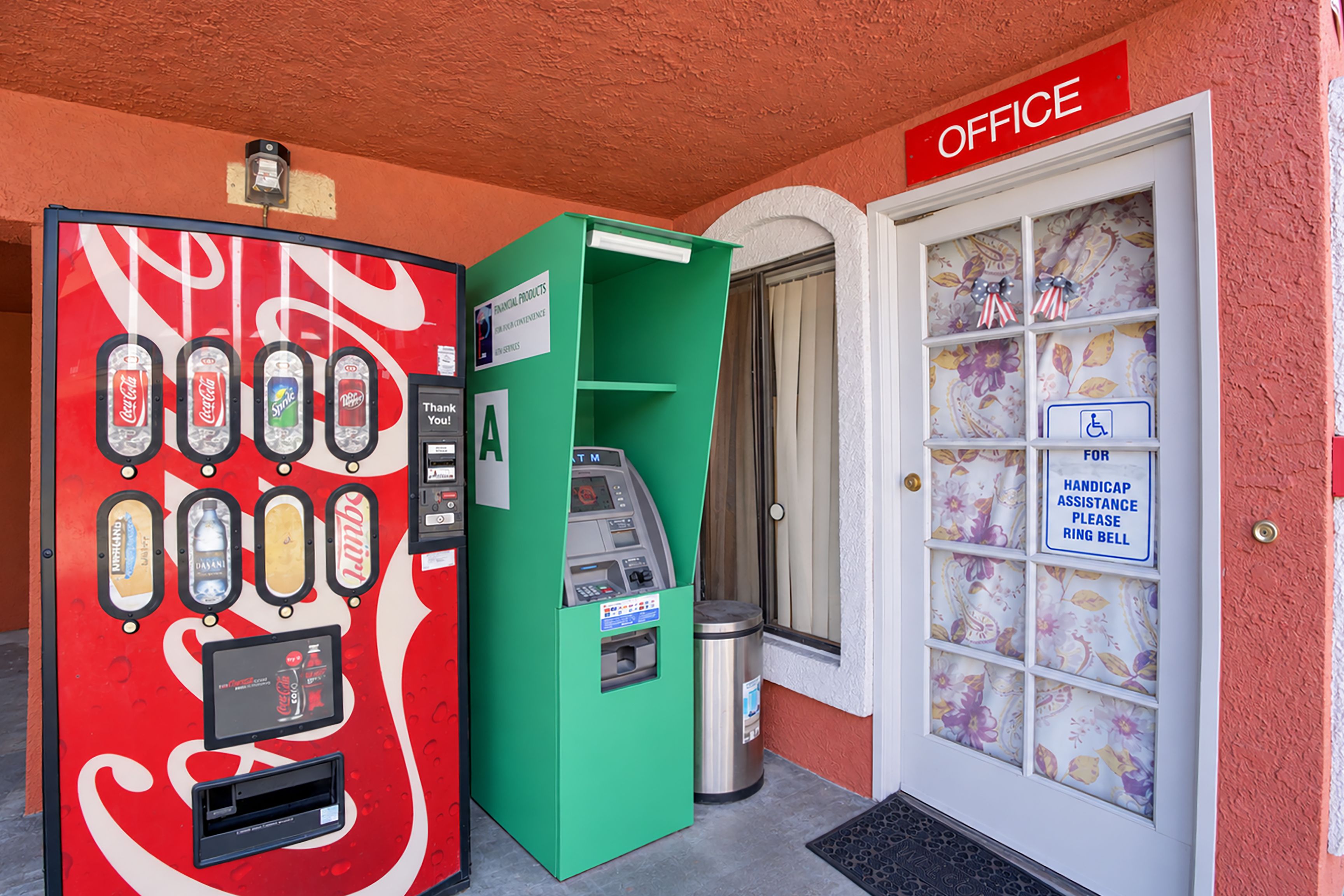 A vending machine with various drink options and a green ATM machine next to a door labeled 'OFFICE'.