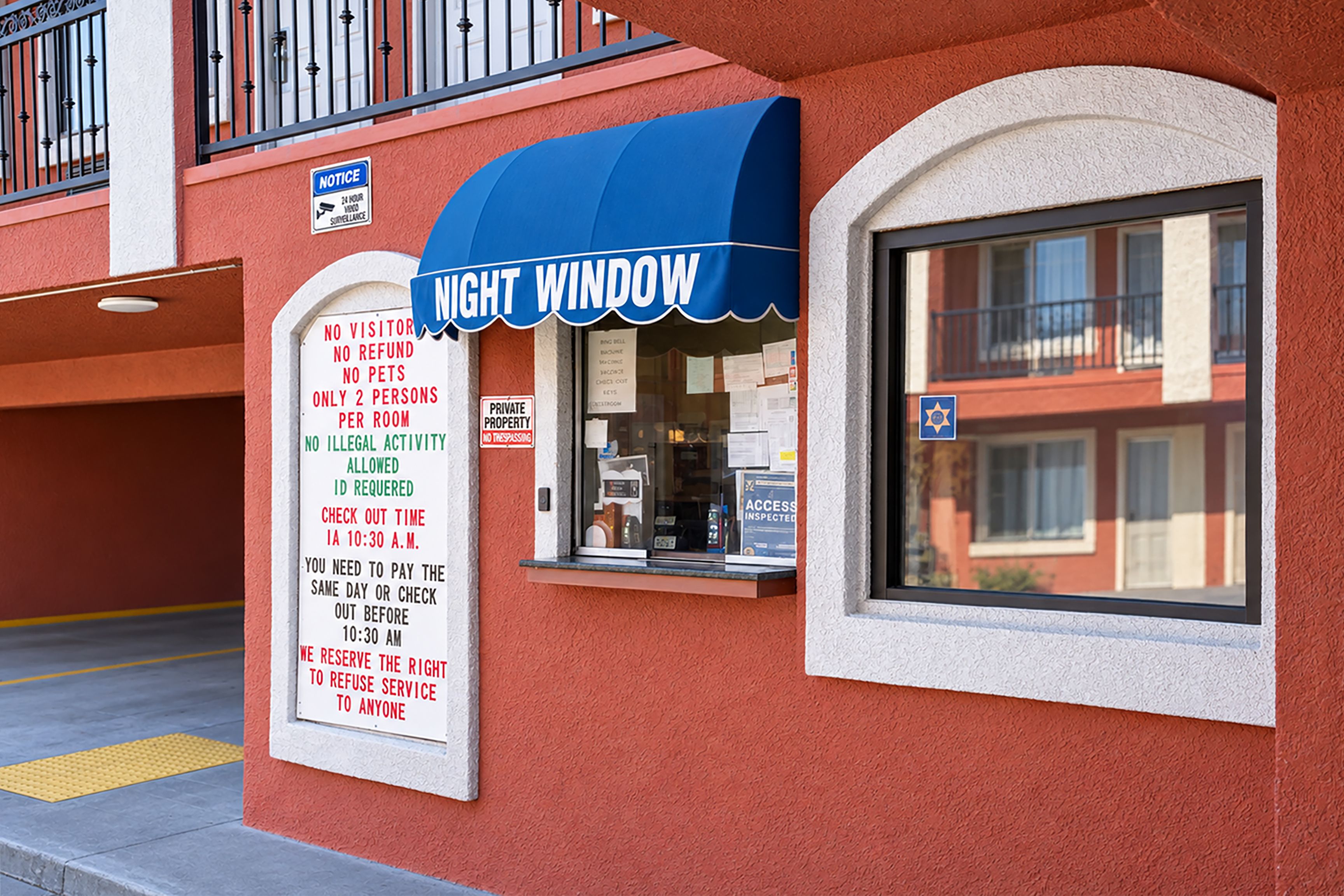 A building with a blue awning and a sign indicating 'No Visitor, No Refund, No Pets, Only 2 Persons Per Room, No Illegal Activity, ID Required, Check Out Time 10:30 A.M., Same Day Payment or Check Out Before 10:30 A.M., We Reserve the Right to Refuse Service to Anyone.'