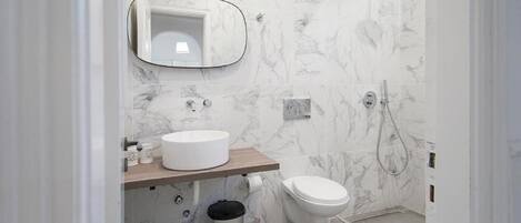 A modern bathroom with a marble backsplash, a round sink, a toilet, and a shower.