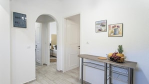 A hallway with a kitchen area in the background, a fruit basket on a table, and two framed pictures on the wall. - Alexia studios (Skiathos)