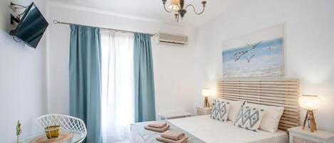 Un dormitorio con cama, lámparas de noche, televisión, una silla y ventana con cortinas.