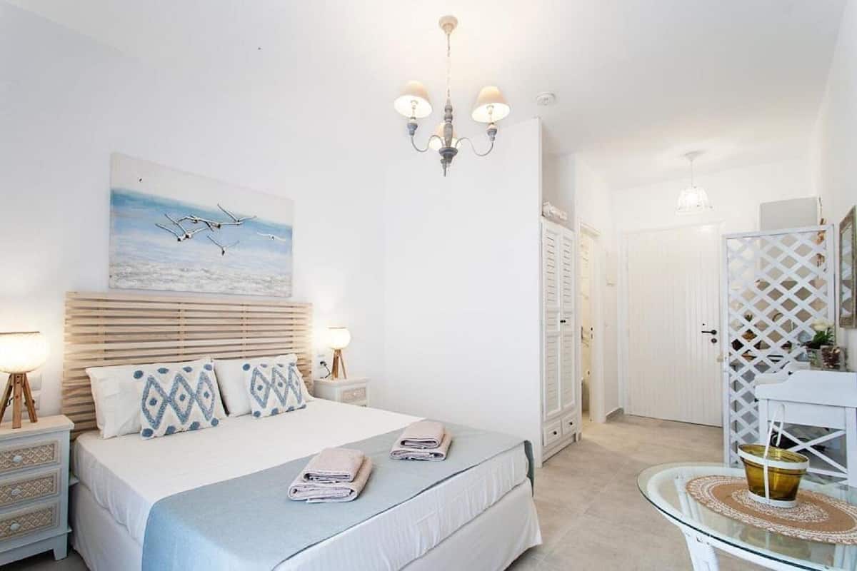 Un dormitorio con cama, mesitas de noche, candelabro, un cuadro y un baño con espejo y lavamanos.