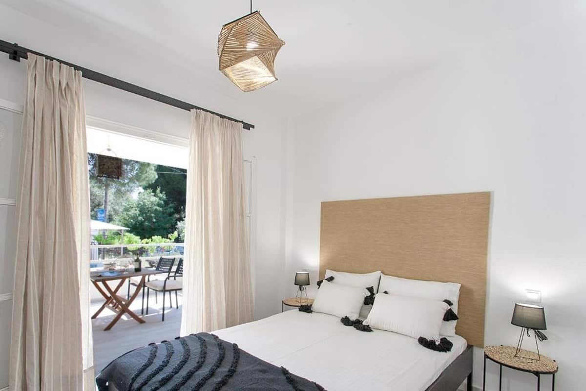 Un dormitorio con una cama grande, cabecera de madera y vistas a un patio exterior con mesa y sillas.