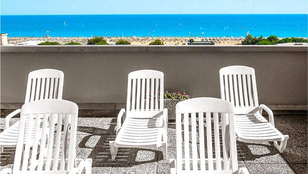 Three white lounge chairs facing a beach with a clear view of the ocean.