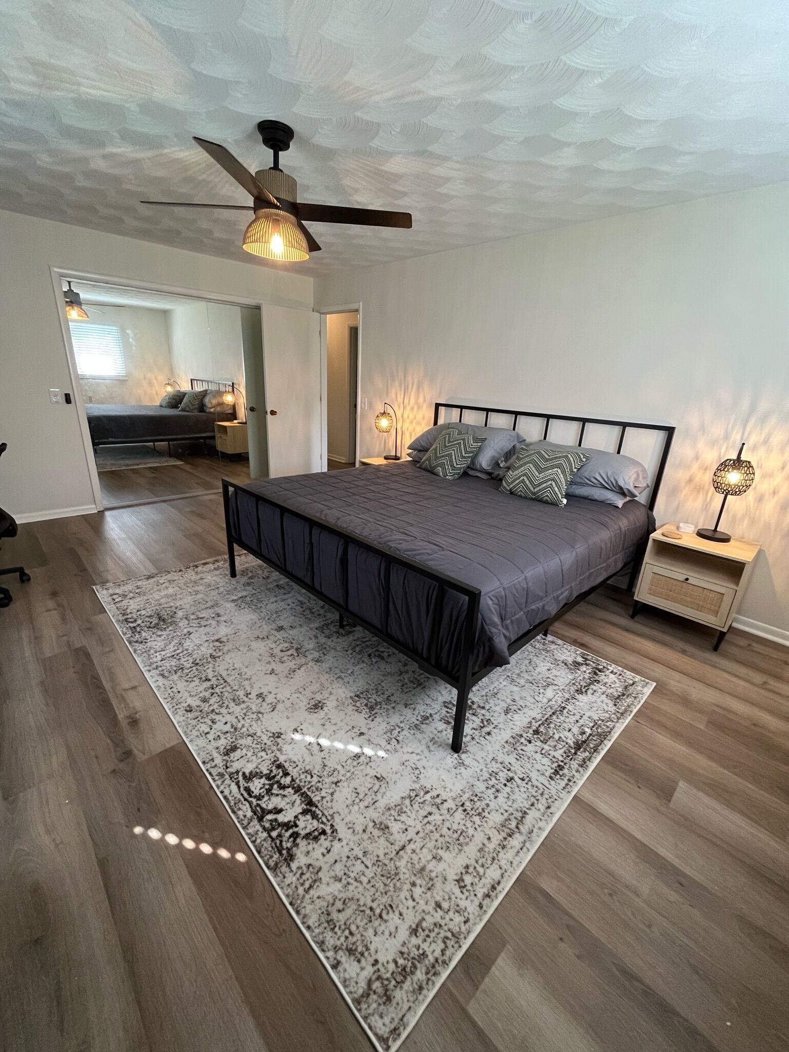 Une chambre à coucher avec un lit, un ventilateur de plafond, une table de chevet et un tapis.