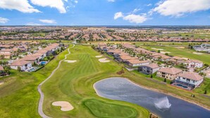 A golf course with sand bunkers, a pond, and residential houses.