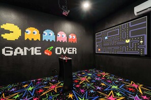 A room with a black wall featuring a 'GAME OVER' sign and pixelated characters, a colorful star-patterned floor, and a projection screen displaying a maze. - Elite 9BR Disney Villa | Home Theater and Pool (Davenport)