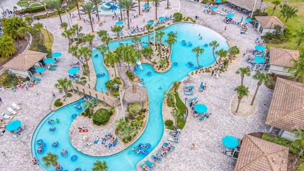 An aerial view of a resort with a winding pool, palm trees, and sun loungers.